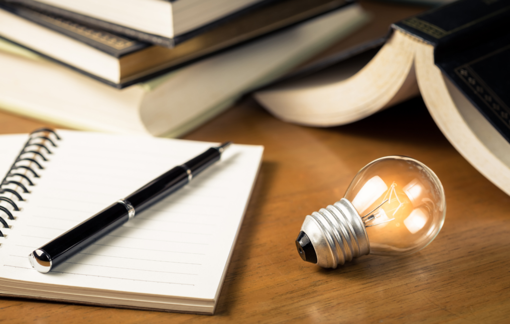 open notebook and pen next to lighted bulb